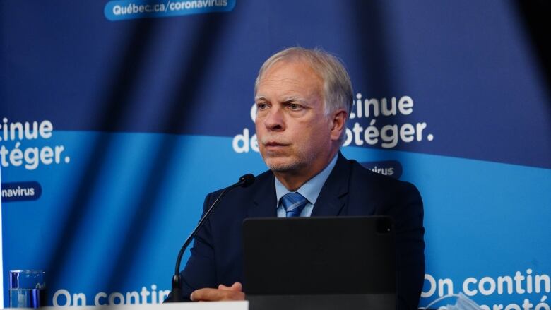 A man seated behind a microphone and a laptop. 