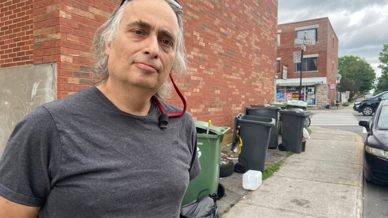 A man stands on a residential street littered with trash. 