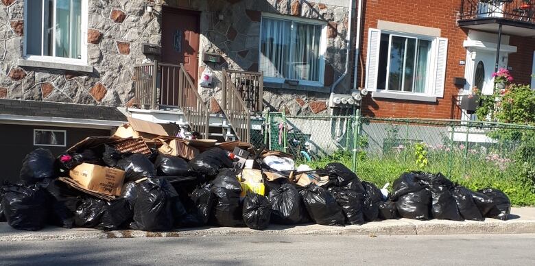 Dozens of trash bags pile up infront on a residential street. 