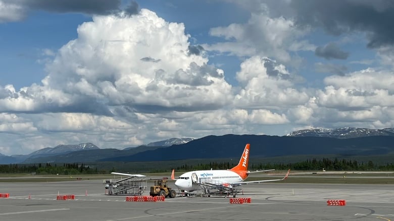 An airplane sits on the tarmac with mountains in the background.