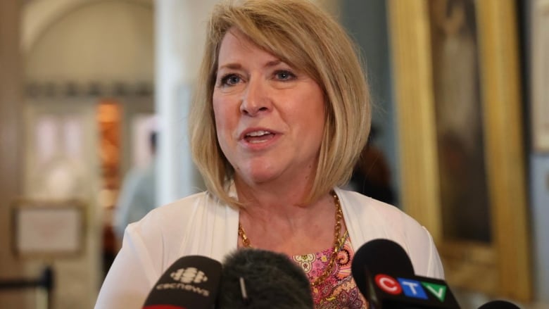 A woman with short blond hair speaks into multiple microphones.  