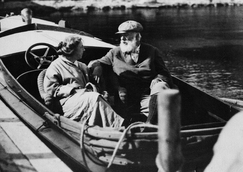 A woman and a man sit in a docked motorboat in a black and white photograph. 