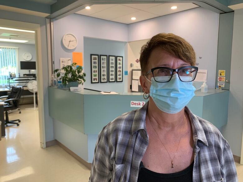 Middle-aged woman wearing a face mask and glasses stands in front of the reception desk at the clinic in Grandview.