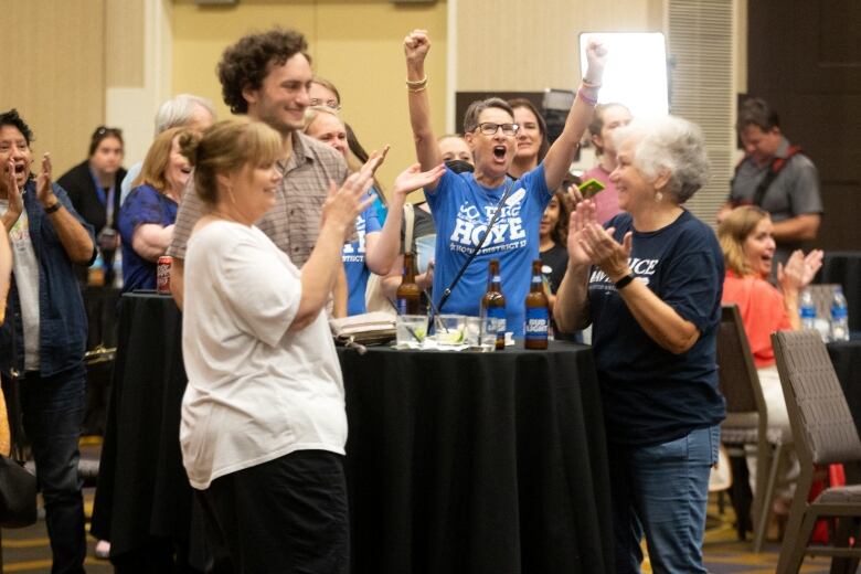 People standing around a table in a hotel conference room rejoice.