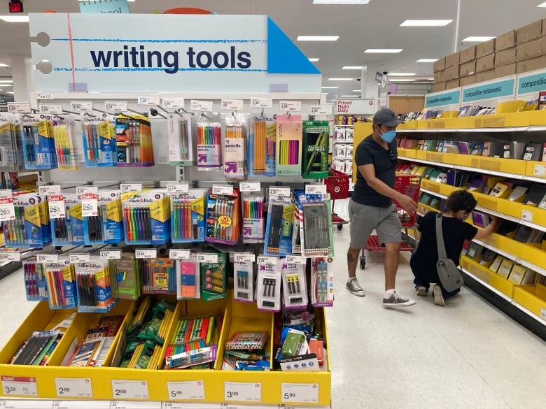 Two people wearing masks examine school supplies in the aisle of a store. 