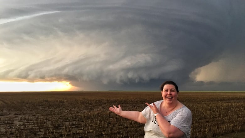 a woman in a white shirt in front of a large cloud and empty field. 