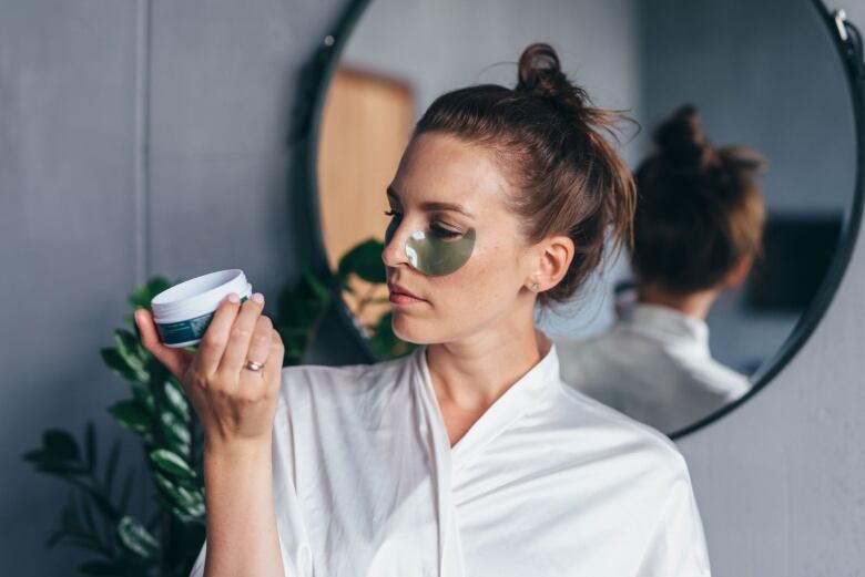 A woman applies cream to her face.