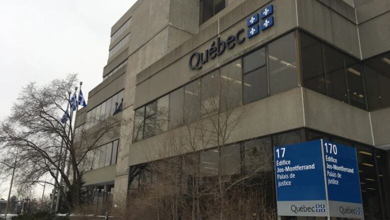 The Jos-Montferrand Building, a grey concrete building with blue signage indicating the provincial courthouse in Gatineau, Que. Photo on a winter day with leafless trees around the building. 