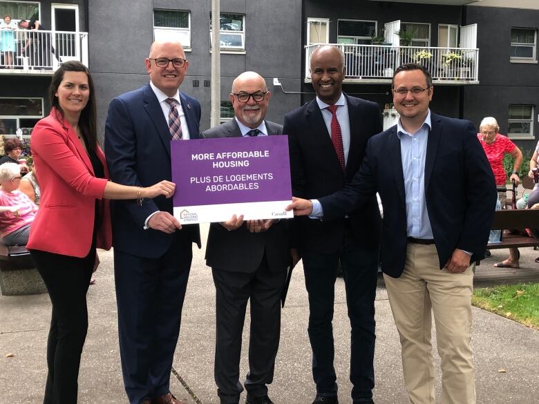 Five people holding a purple sign that says more affordable housing.