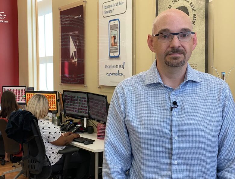 Stephen Sauer standing in his office with people working on computers behind him.