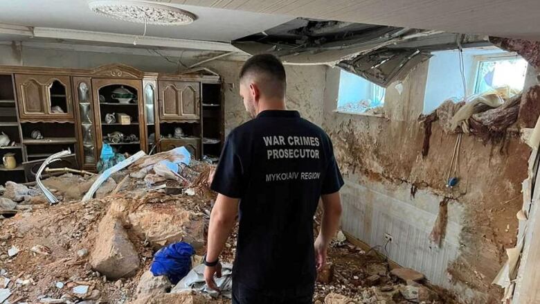 A man with his back turned standing inside the rubble of a building.