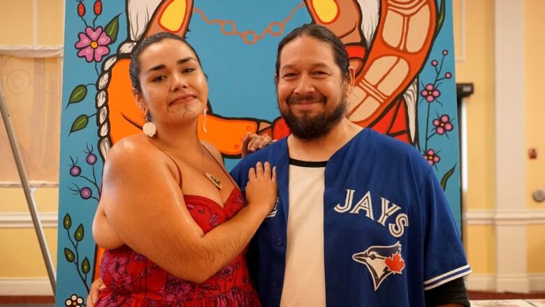 A woman stands with her arms around a man in front of a painting.