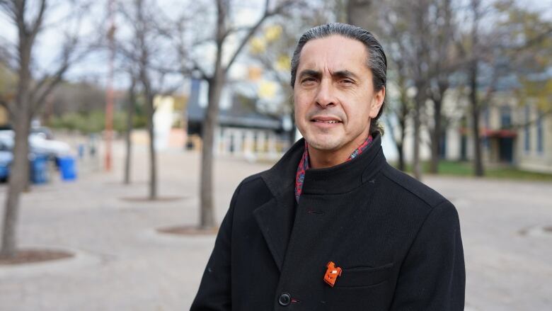 A man with a grey ponytail and a black jacket looks to the camera.