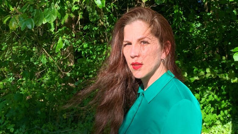 A portrait of a woman with dark brown hair looking over her shoulder into the camera.