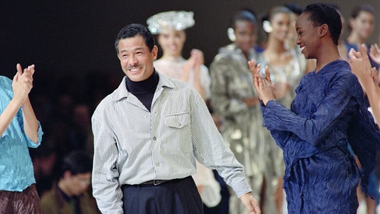 Several people smile and clap on a fashion runway.