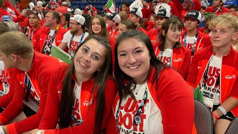 Two women wearing white and red smile. They are sitting in a crowd of people all wearing the same thing.