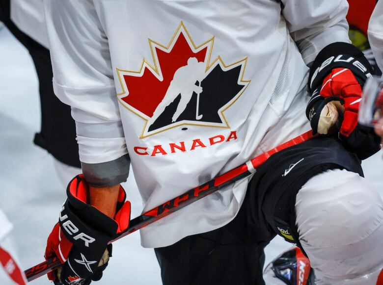 A closeup of a player wearing a Hockey Canada jersey, and wielding a hockey stick. 