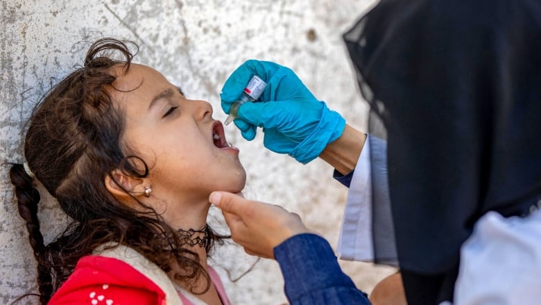 A young girl gets a vaccine from a small vial and a dropper.