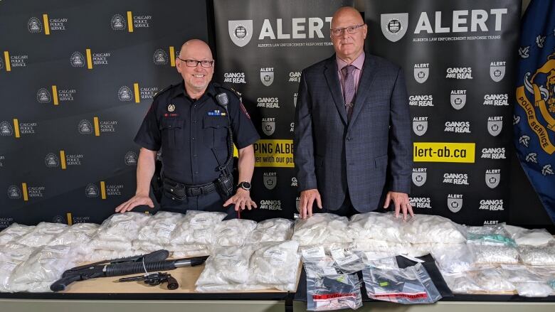 two men standing with their hands over bags of white powder 