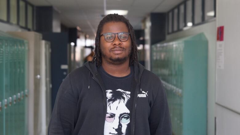 A man stands in hallway with lockers. 