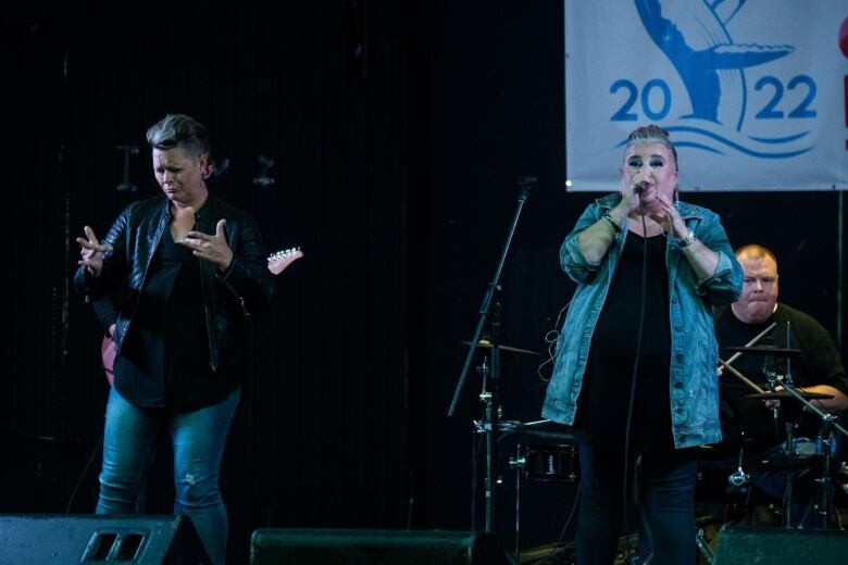 A singer preforms on stage with an American Sign Language interpreter. A drummer sits behind the singet.