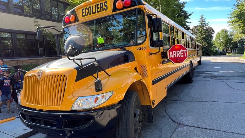 Children are seen embarking on a yellow school bus on a clear summer day.