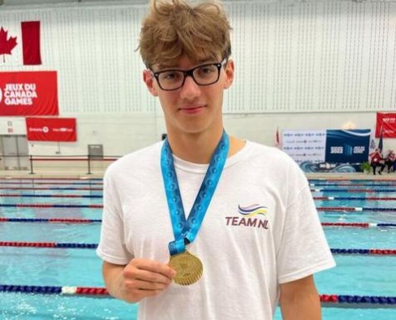 A teenager holds a gold medal in front of a pool