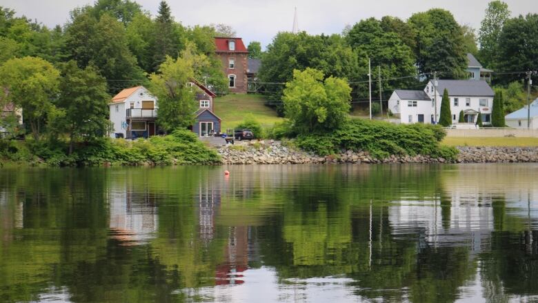 A shot across a river of houses on a grassy hill, they reflect in the water.