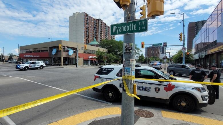 Police cars block a downtown intersection with cars and caution tape.