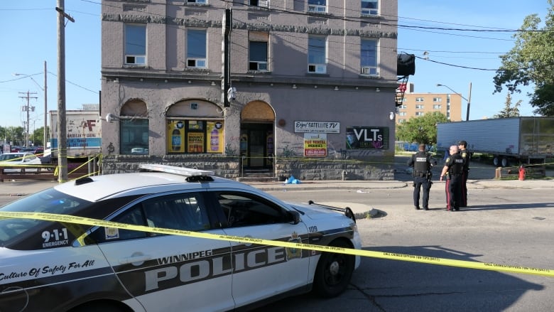 Three police officers are pictured outside a brick building that's surrounded in yellow tape. A police cruiser is pictured in the foregrond.