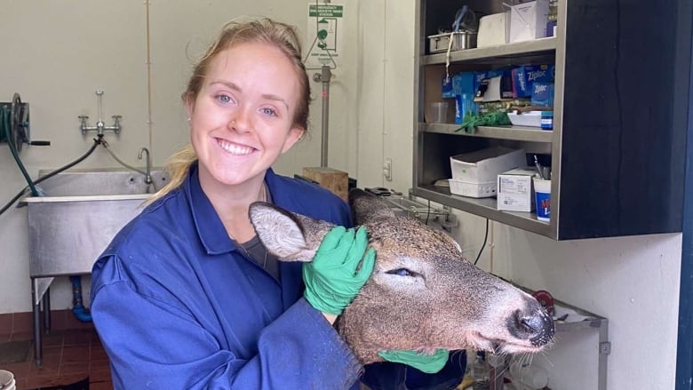 A woman smiles as she holds up a deer head.