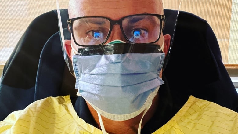 A man dressed in a mask and a hospital gown takes a selfie. 