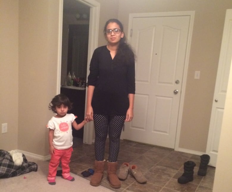 A woman and a girl stand inside an apartment.