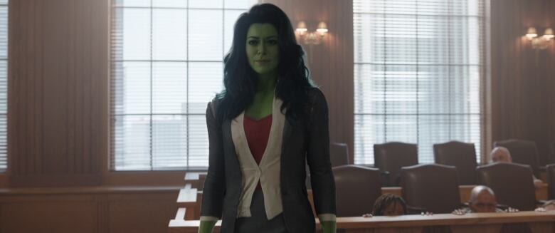 A green-skinned woman stands in front of a courtroom's empty jury box. 