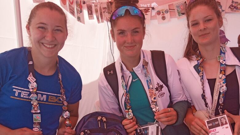 Three women face the camera wearing lanyards covered in decorative badges. They are smiling.