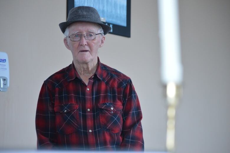 An elderly man stands in the background inside a church with a candle in the foreground.