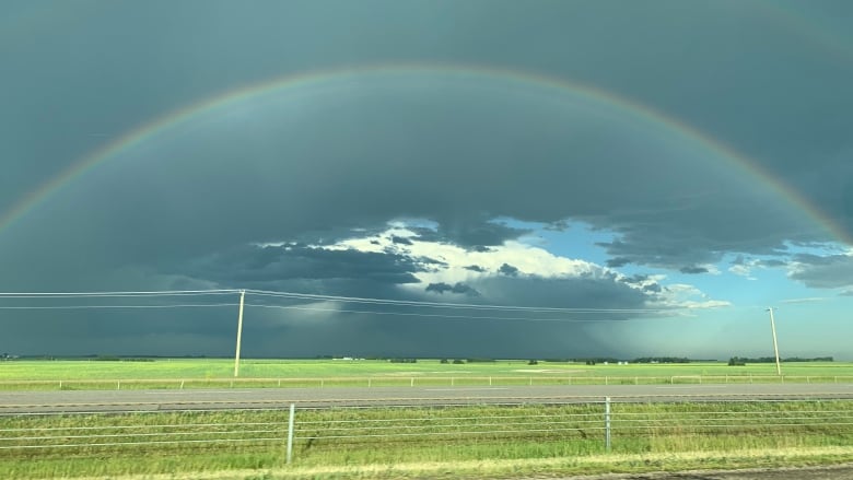 A rainbow with a dark storm cloud behind it and bright grass underneath. 