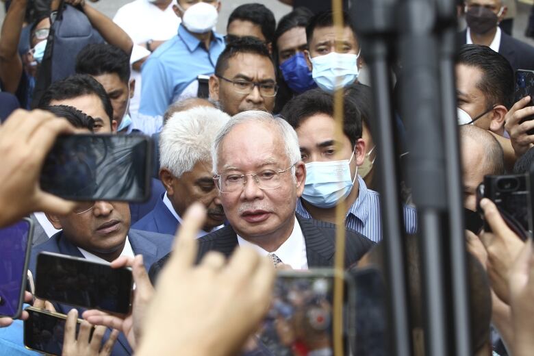 An older man is shown outside surrounded by several people.