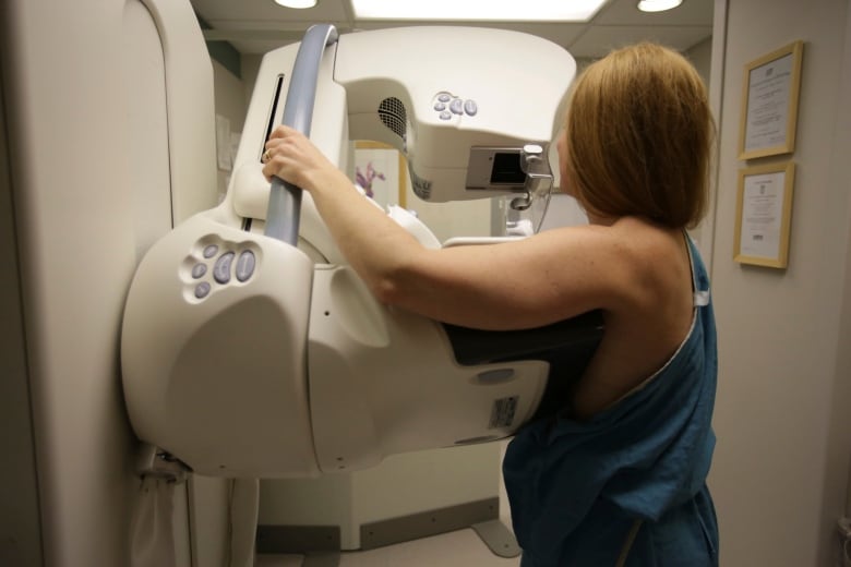 A person, seen from the back, gets a mammogram. The mammography machine is a large, white and grey machine at chest level.