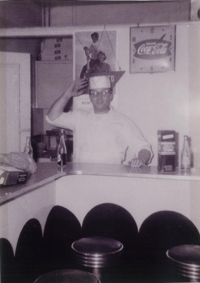 A cook waves from behind the counter of a restaurant.