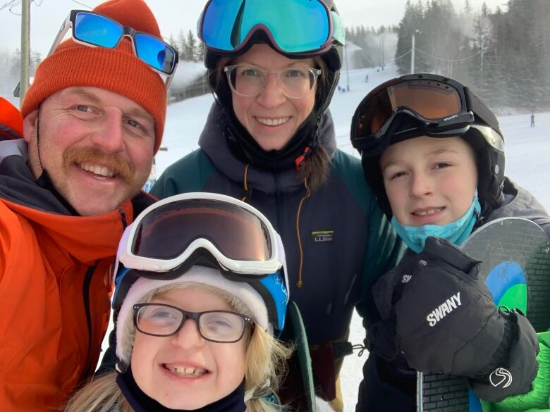 Family smiling, wearing ski goggles and hats. 