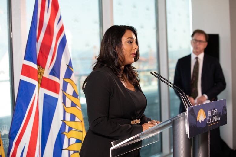 Dr. Ramneek Dosanjh talks at a podium marked British Columbia, with the B.C. flag behind her. She is a South Asian woman wearing a black dress.