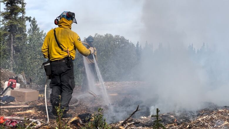 Firefighter holding a hose lays pumping water on burning fire.