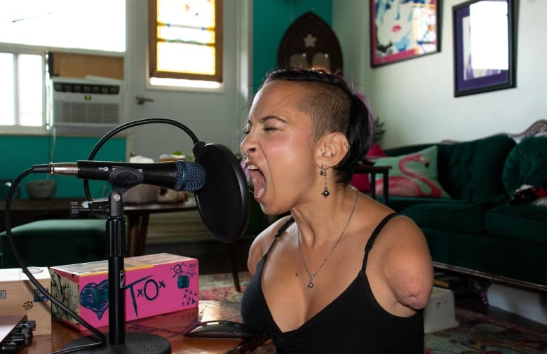 A woman with a half a shaved head and facial piercings screams into a microphone. 