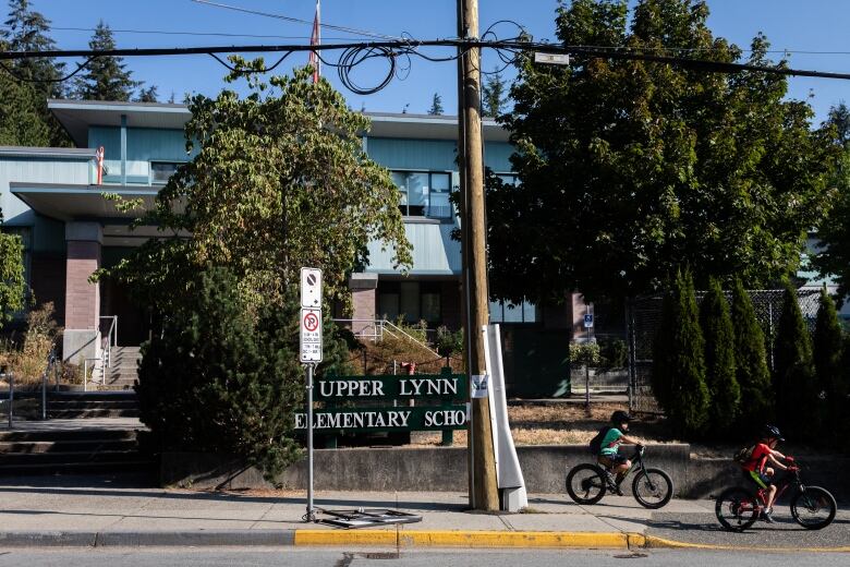 The exterior of Upper Lynn Elementary School, with two children on bikes on the nearby pavement.