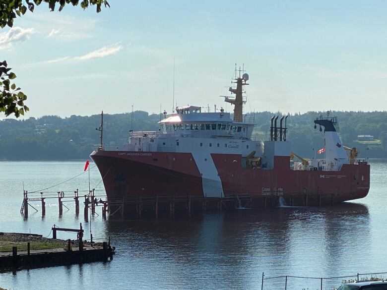 The Canadian Coast Guard offshore fisheries science vessel CCGS Jacques Cartier is seen near a small dock. The hull of the boat is red while the upper portion is white.