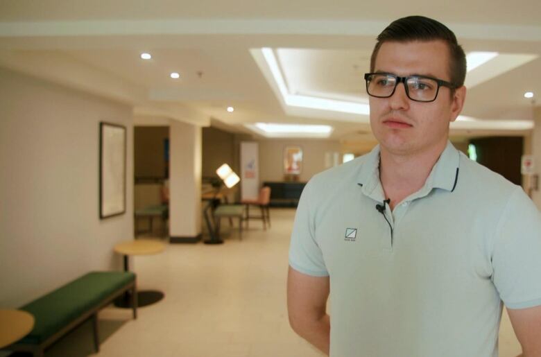 A young man wearing a polo shirt stands in a hotel lobby