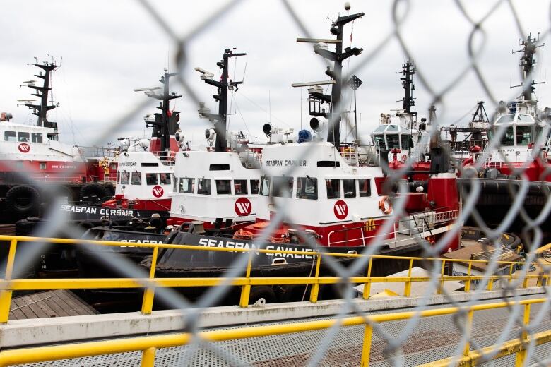 A row of Seaspan-branded tugboats lie unmanned in a pier.