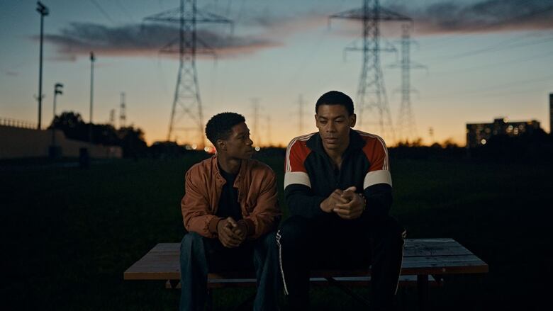 Two young men sit side by side on a picnic table at sunset.