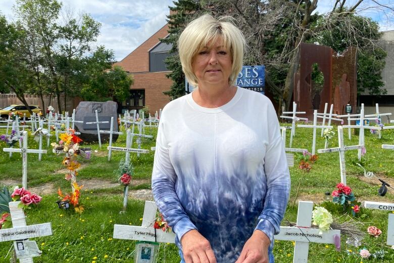 A woman stands in a field with white crosses.